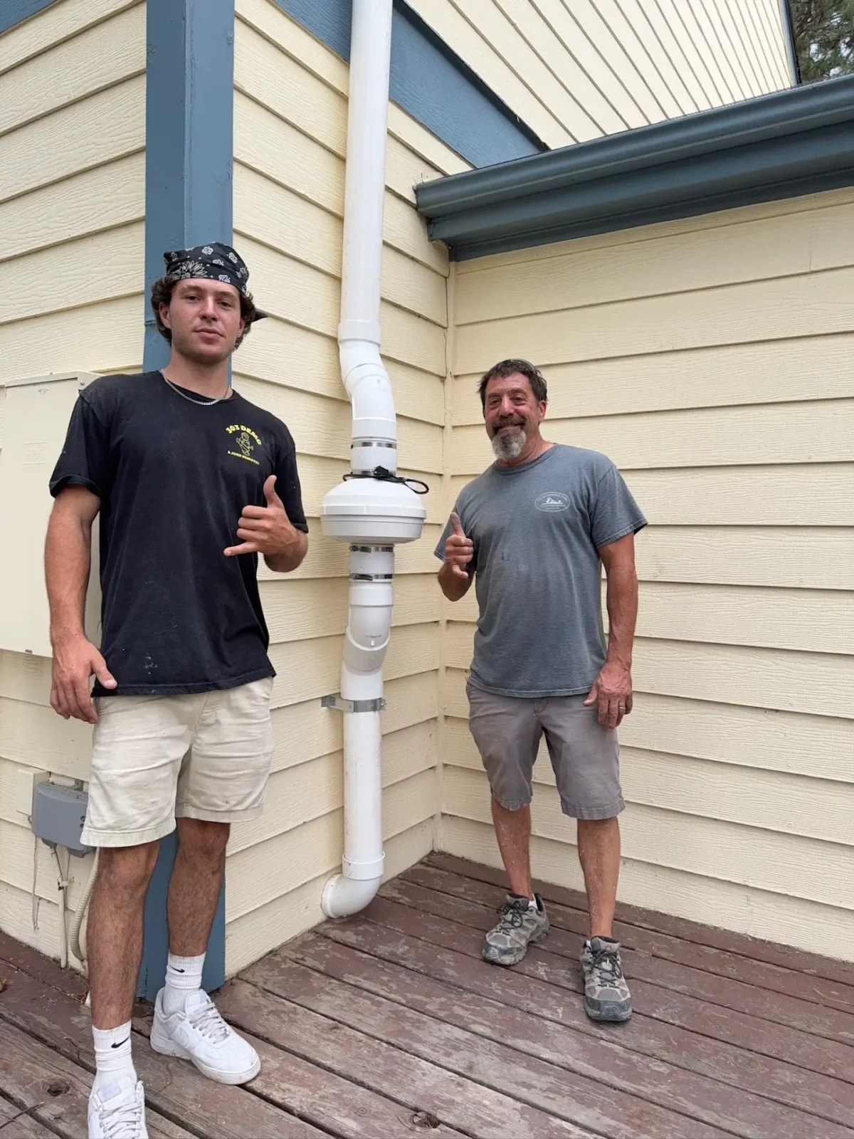 Ty Silver and his father beside a radon mitigation vent pipe on a Lafayette, CO home