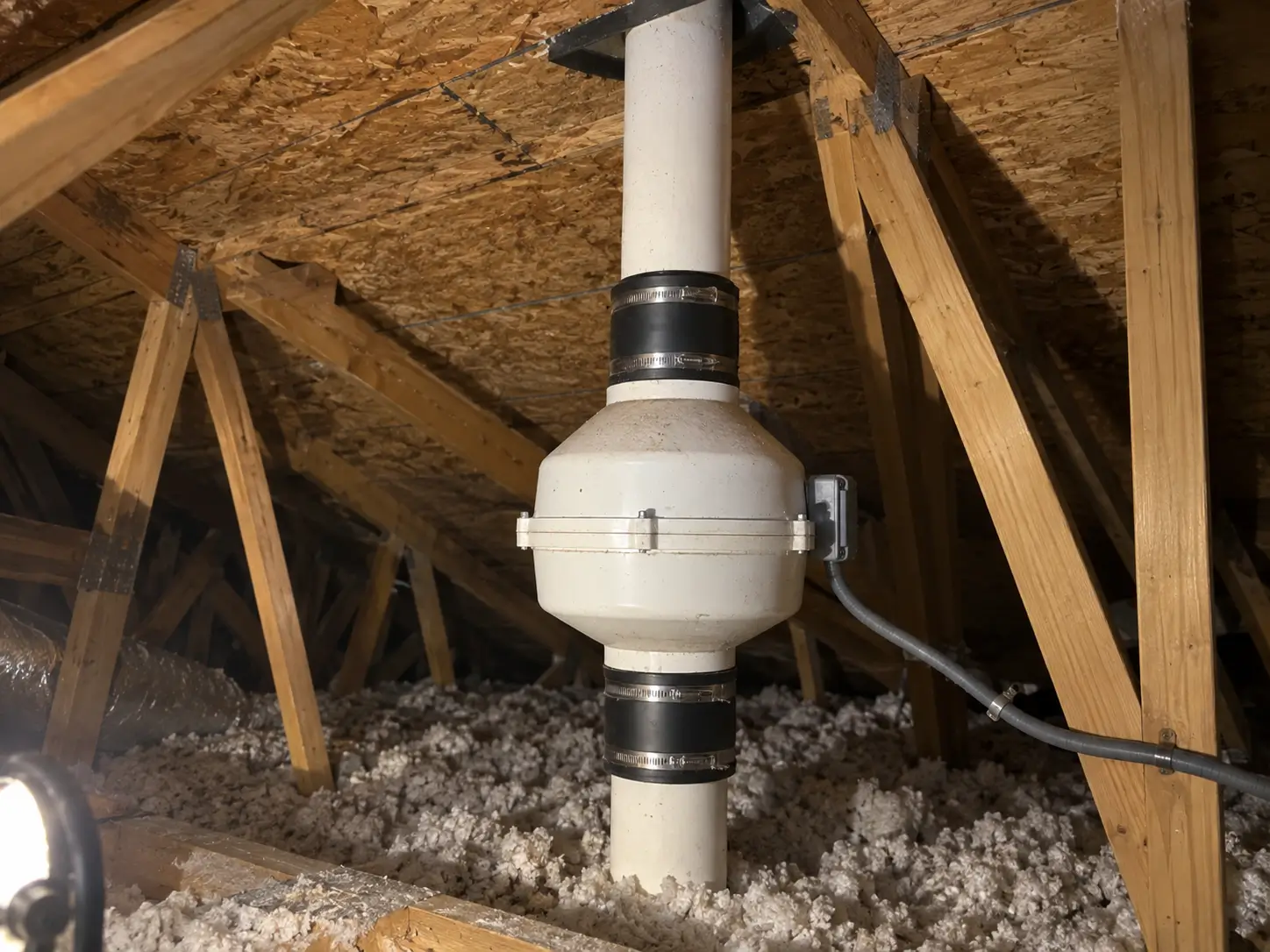 Radon mitigation fan installed inline on the vent pipe in an attic